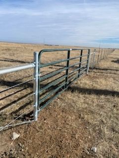 A metal gate is sitting in the middle of a dry grass field.