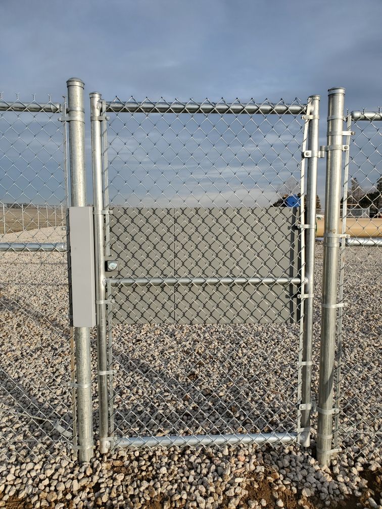 A chain link fence buit by Greater Western Fence  with a gate in the middle of a gravel field.