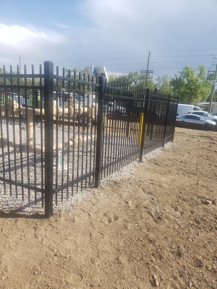 A black metal fence built by Greater Western Fence surrounds a dirt field.