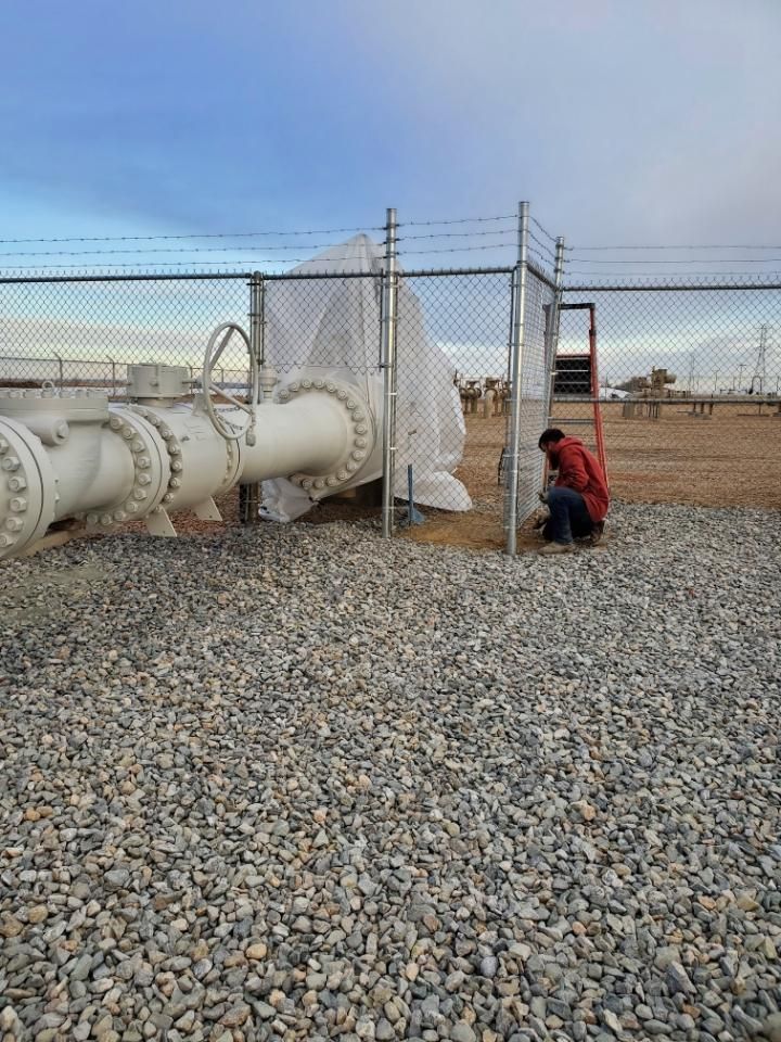 A man is working on a pipe behind a chain link fencebuit by Greater Western Fence