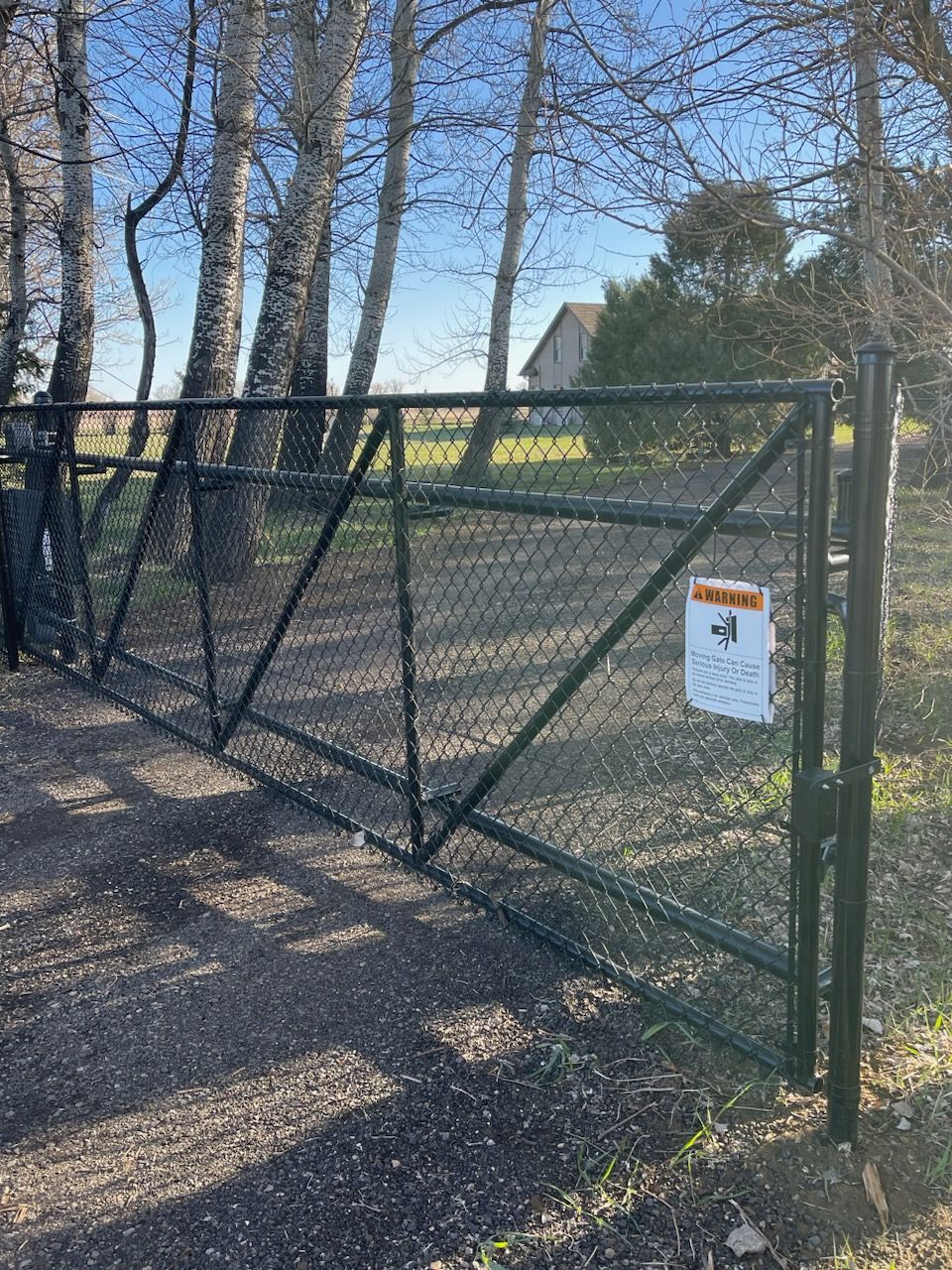 A black chain link fence with a warning sign on it is surrounded by trees.