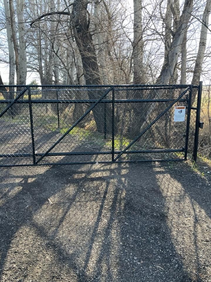 A black metal gate is sitting on the side of a gravel road.