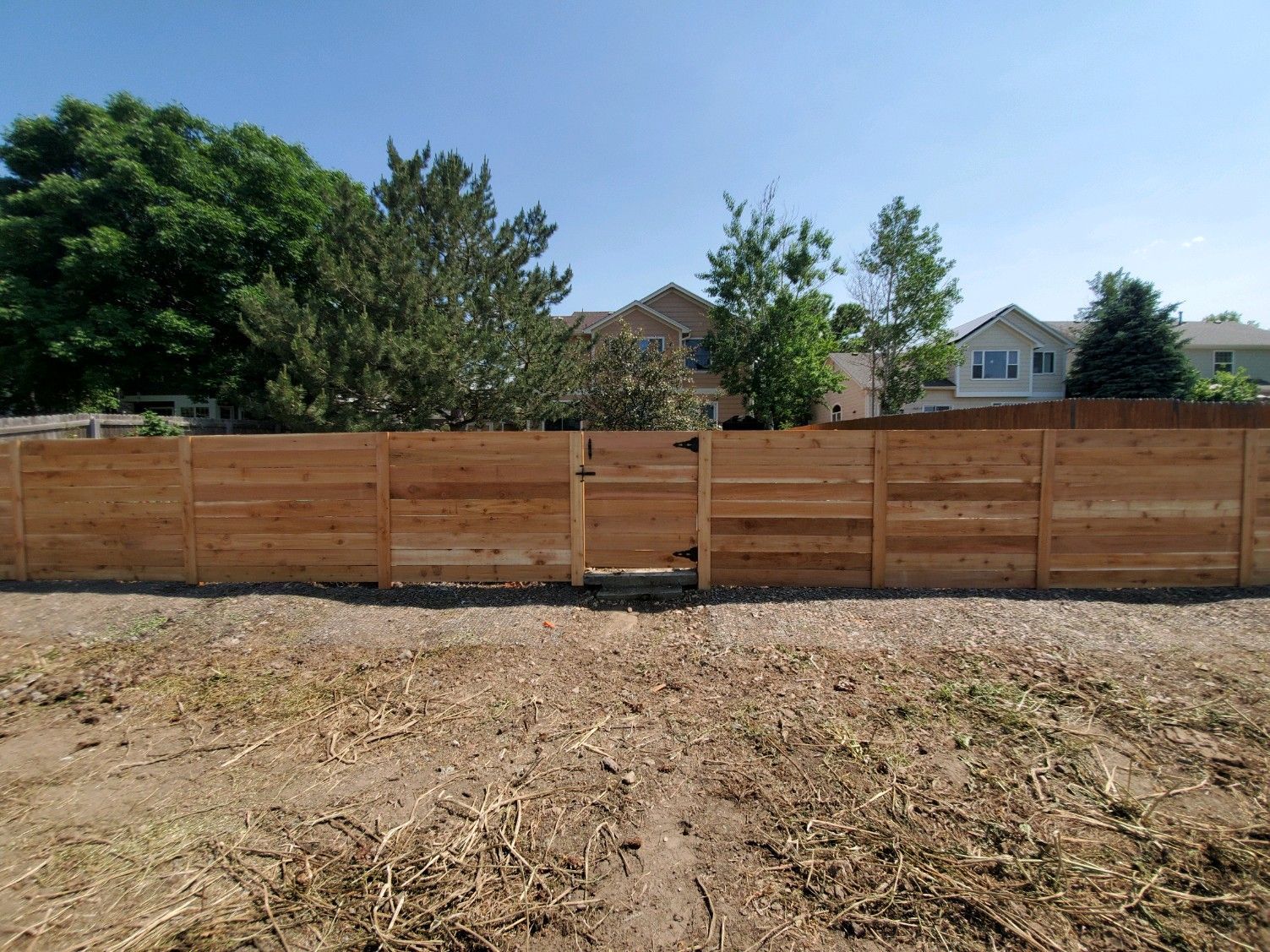 A wooden fence with a gate in the middle of a dirt field.