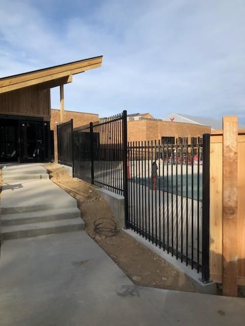 A metal fence built by Greater Western Fence surrounds a swimming pool in front of a building