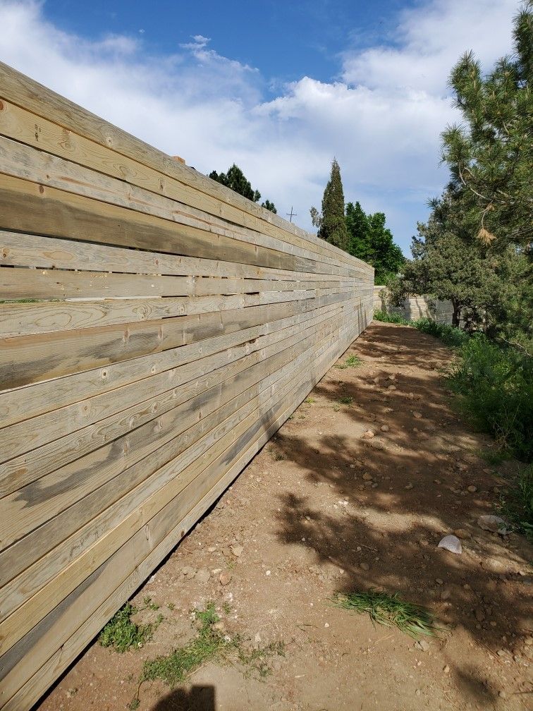 A wooden fence along a dirt path with trees in the background.