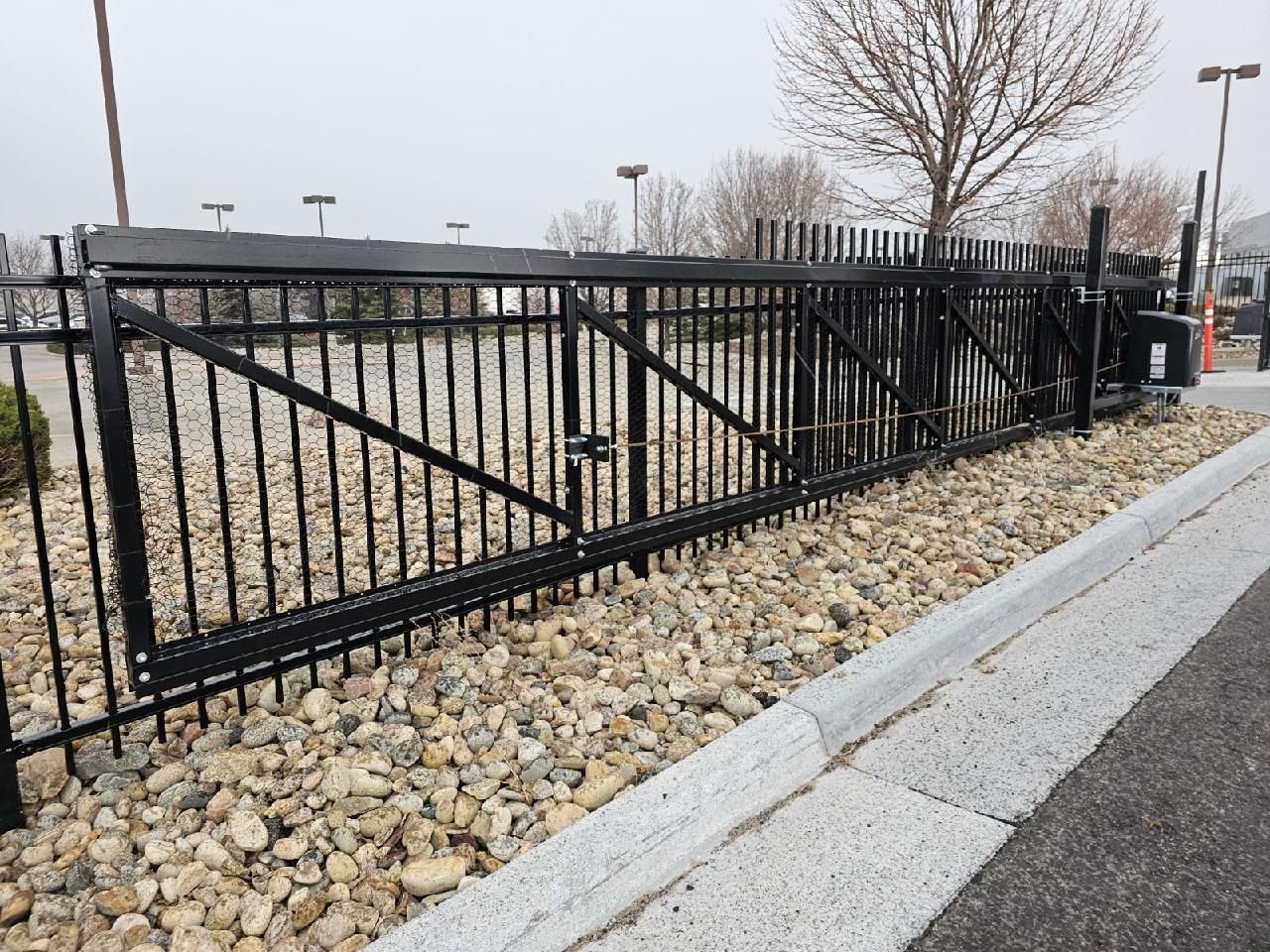 A black metal fence built by Greater Western Fence is surrounded by rocks and gravel.