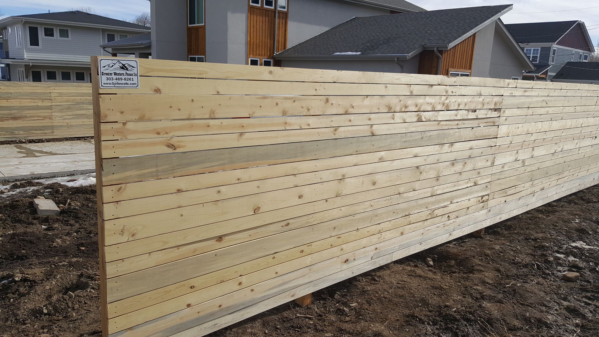 A wooden fence built by Greater Western Fence sits in the dirt in front of a house.