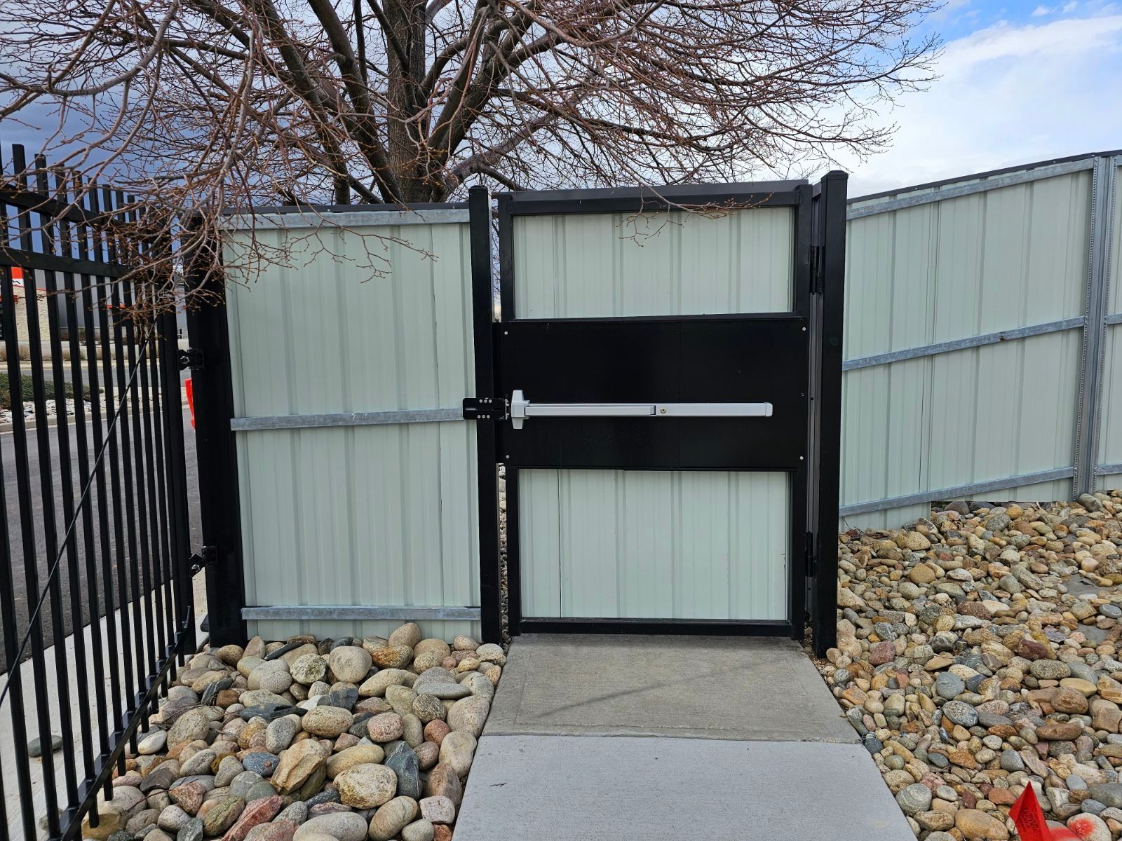 A fence and rocks surround a black and white gate built by Greater Western Fence.