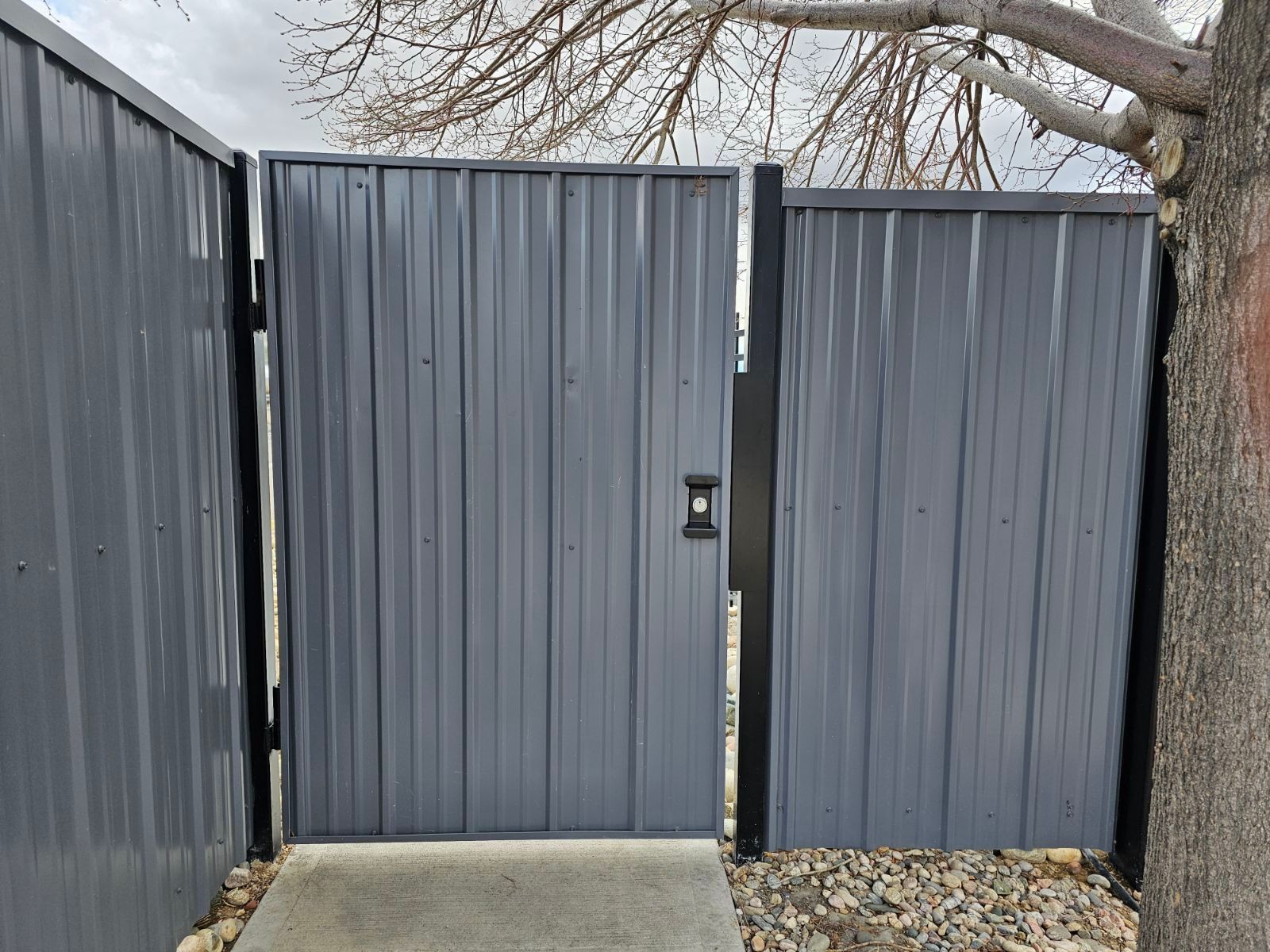 A gray metal gate built by Greater Western Fence with a tree in the background.