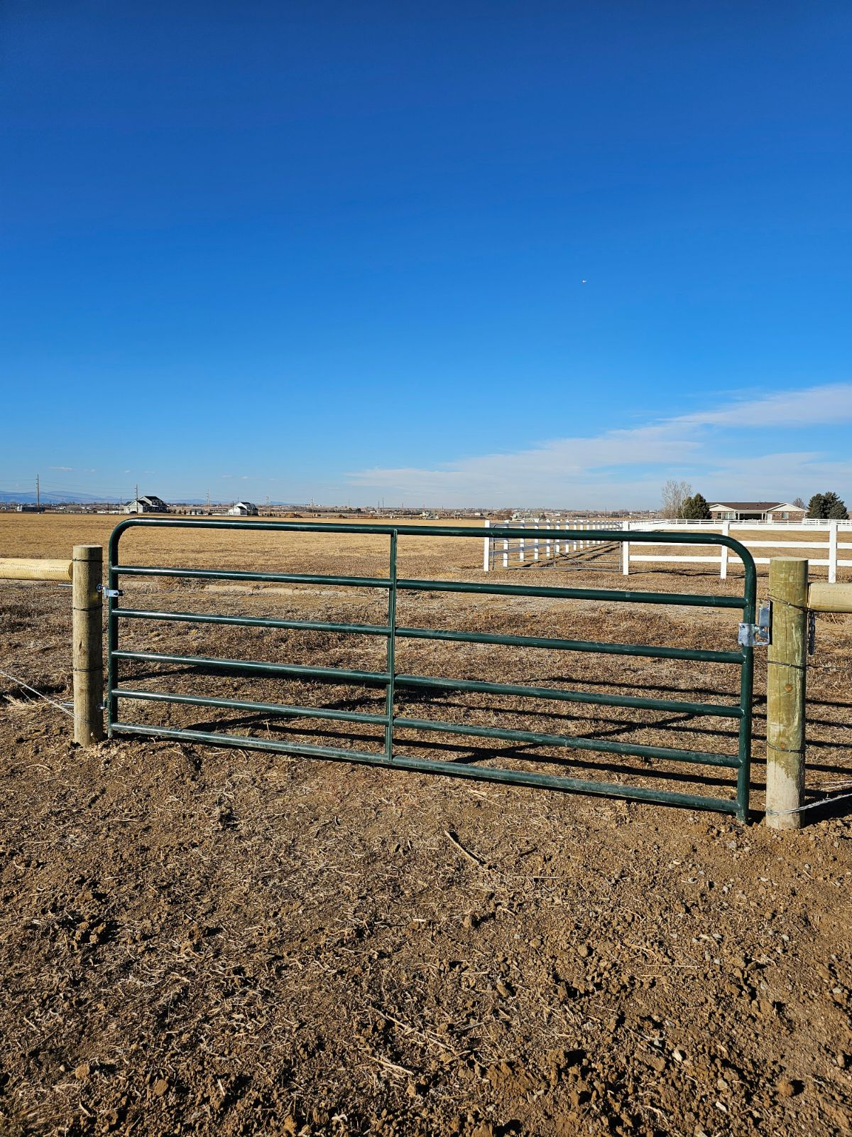 A green livestock gate built by Greater Western Fence sits in the middle of a dirt field.