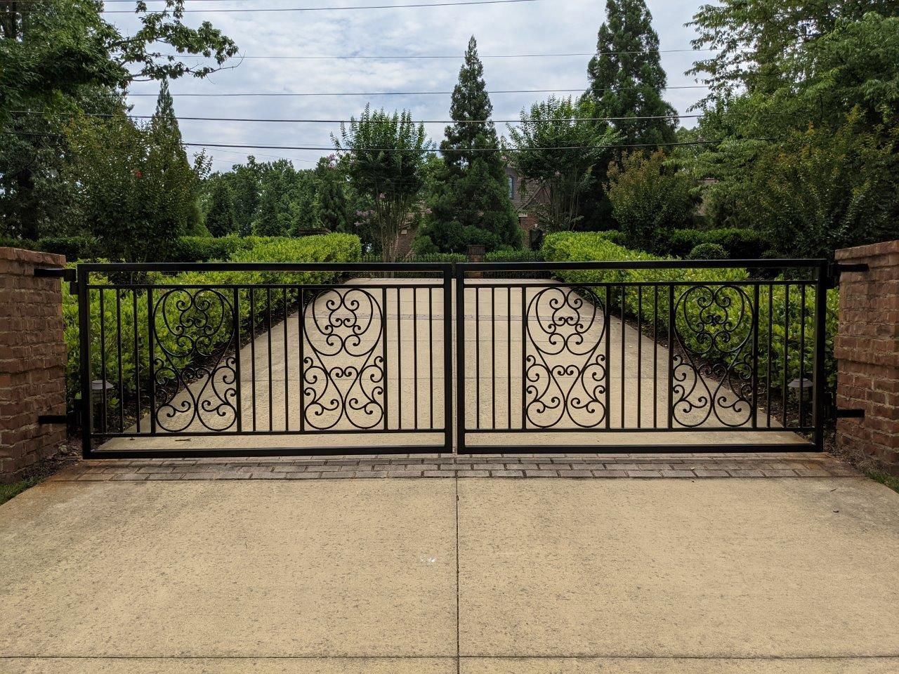 A wrought iron gate built by Greater Western Fence leading to a driveway with trees in the background