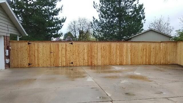 A wooden fence built by Greater Western Fences surrounds a concrete driveway in front of a house.