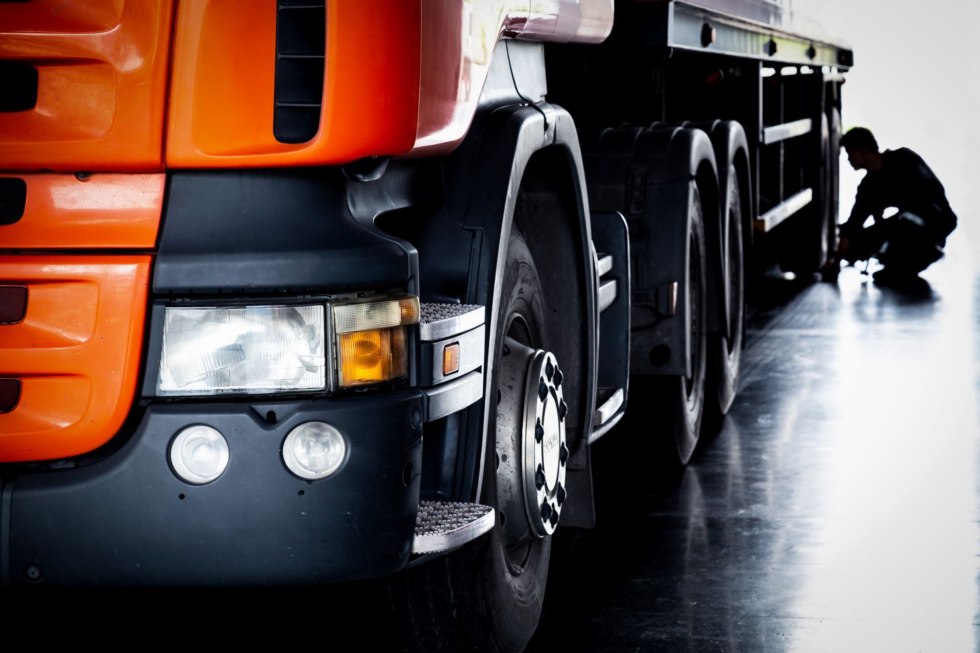 Orange truck with mechanic checking tires in a garage