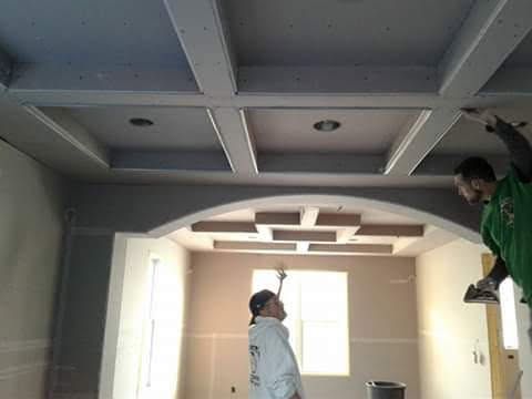 Two workers installing drywall on a coffered ceiling.
