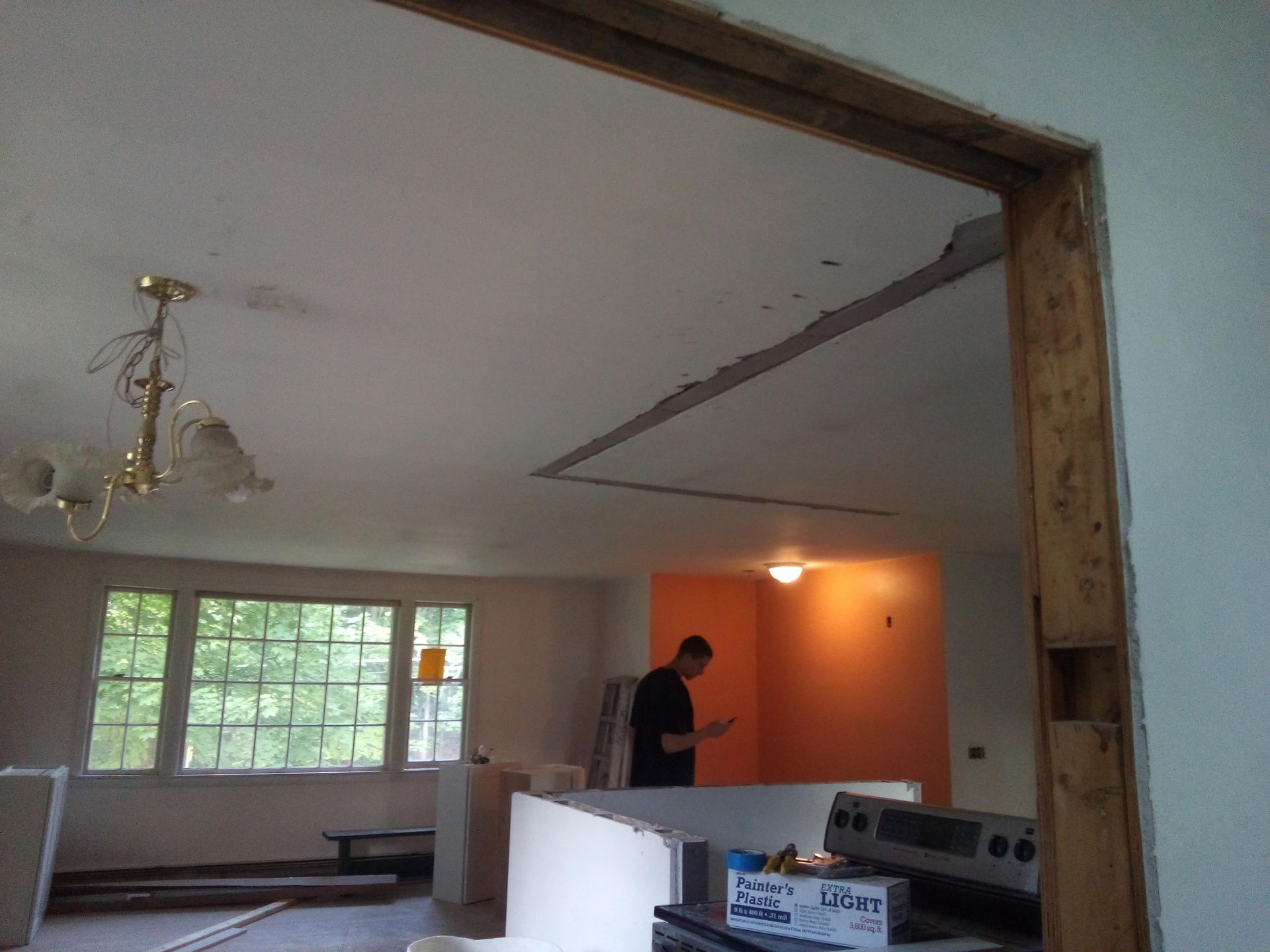 Open doorway with exposed beams, person in room with appliances and partially painted wall.