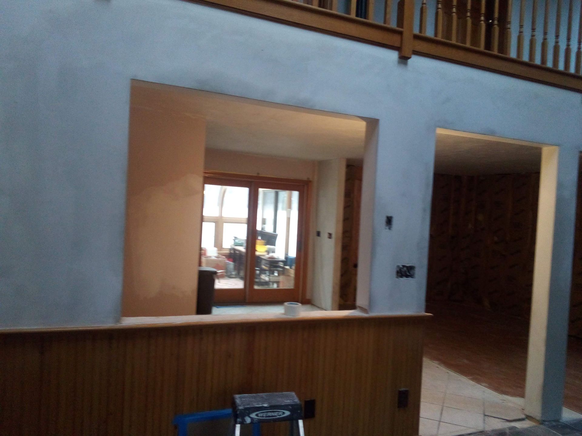 Interior wall with an opening to a room with sliding glass doors; wood paneling on the lower portion.