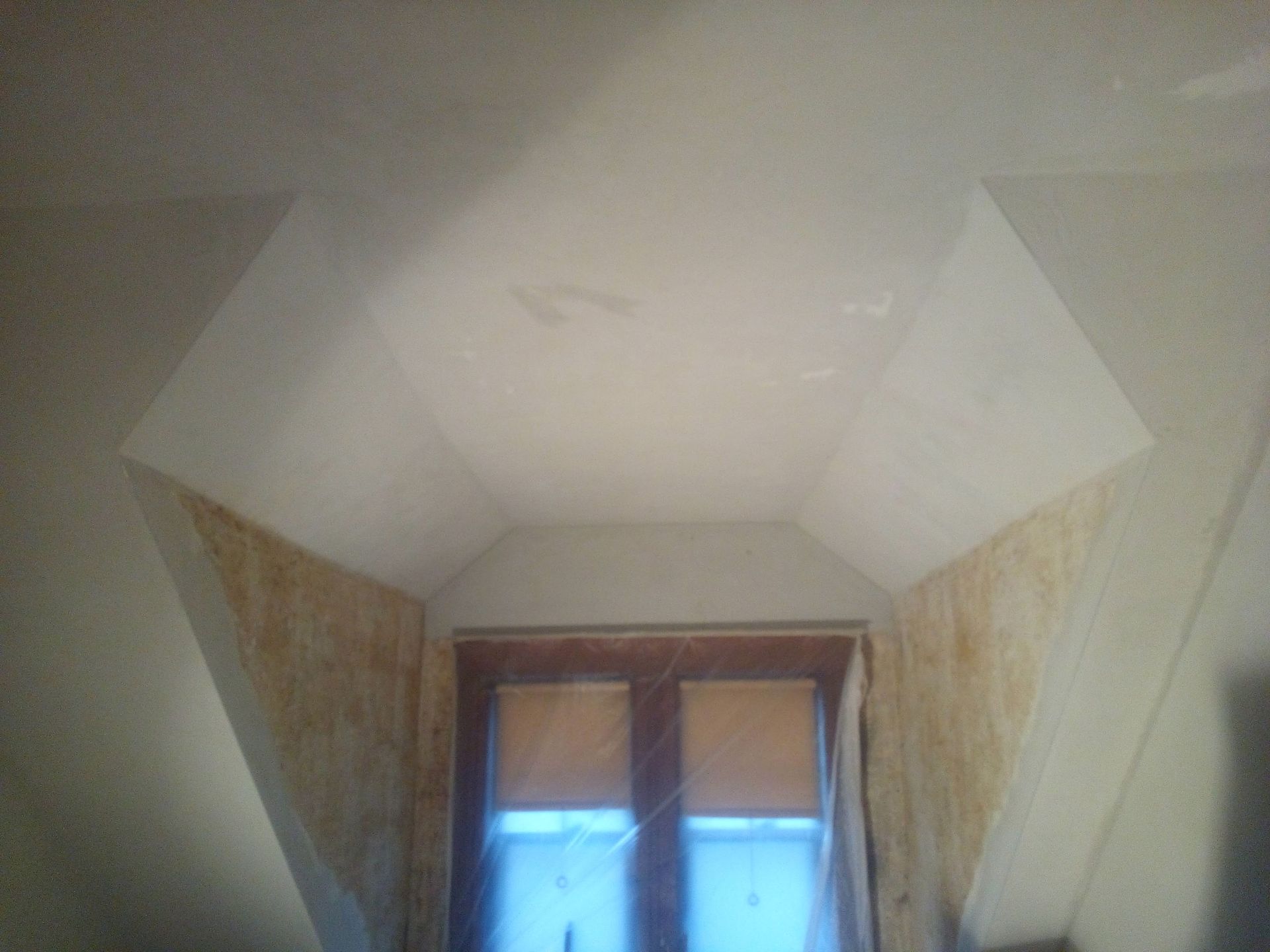 Interior view of an angled ceiling above a window, with white surfaces and some yellowed walls.