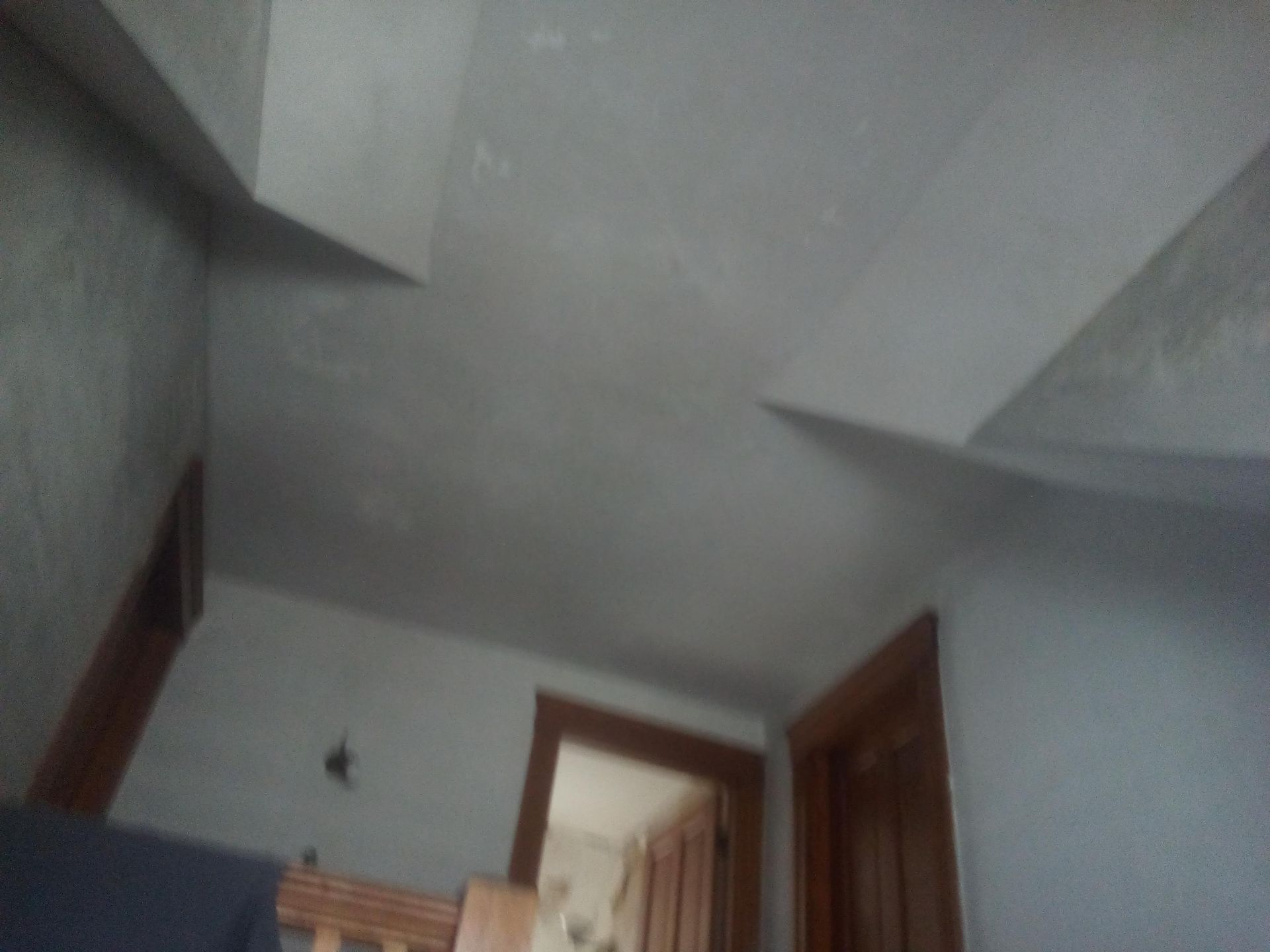 A light gray ceiling with beams, looking up into a hallway with wooden doorframes.