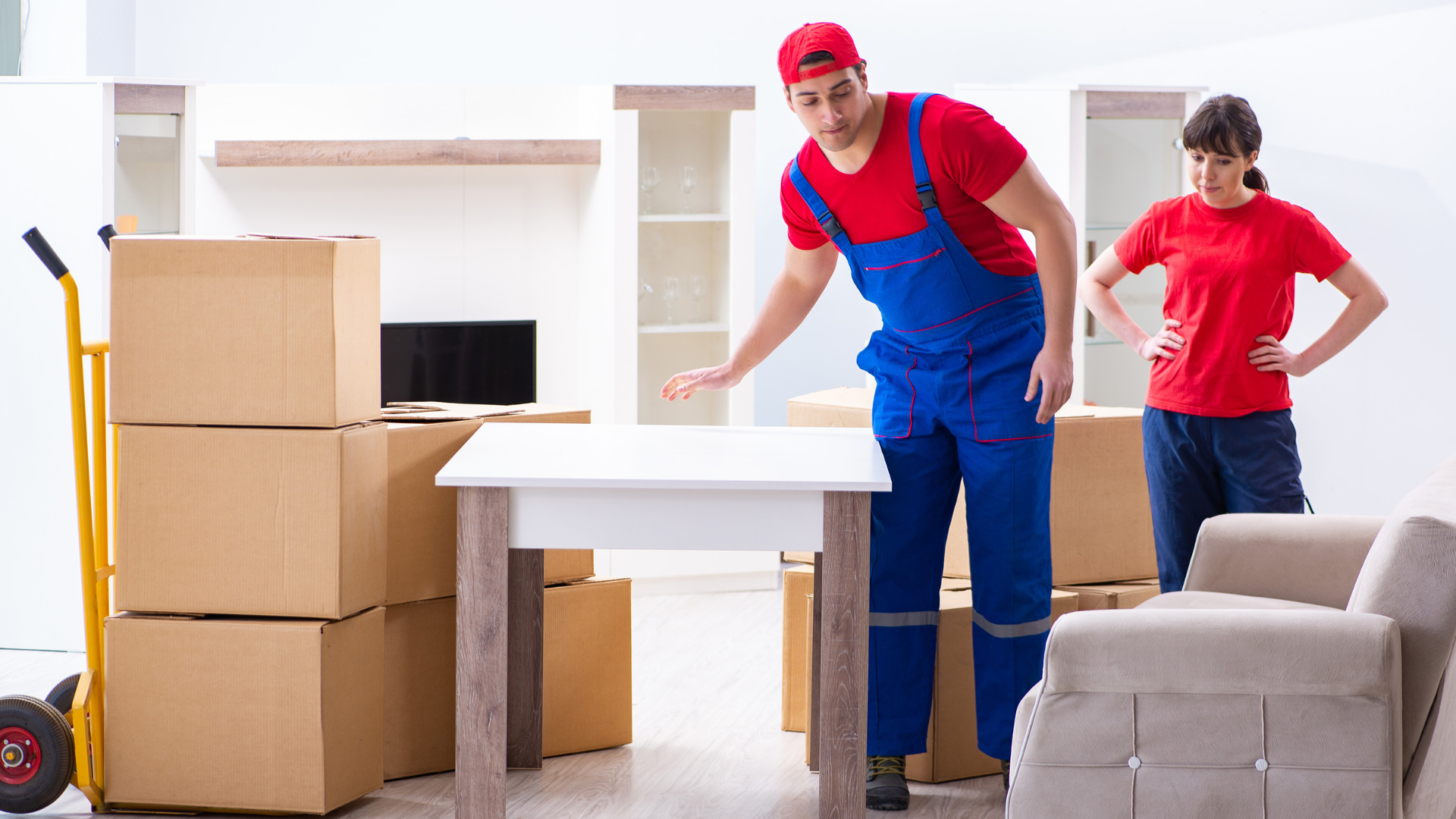 A professional mover helping to move large boxes in an office space while another mover adjusts furniture, highlighting teamwork during a commercial move.
