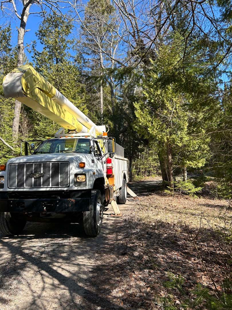 A truck with a crane on top of it is parked on the side of a dirt road.