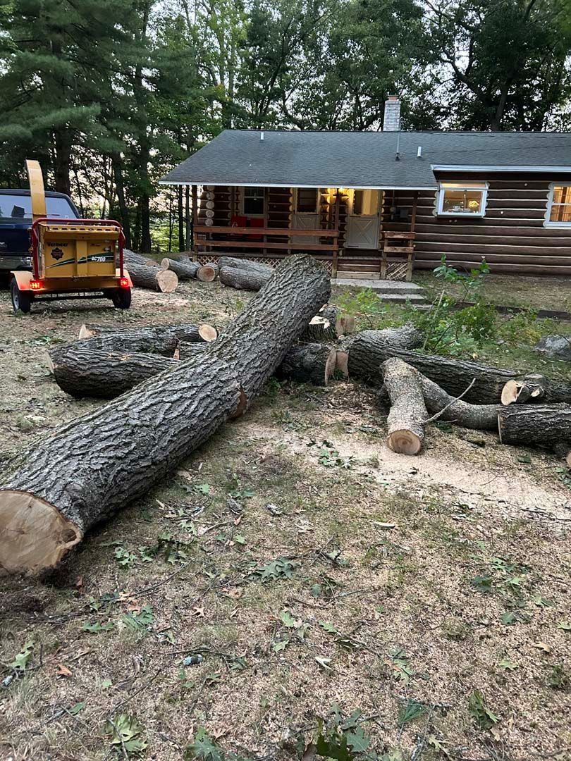 A large log is laying on the ground in front of a log cabin.
