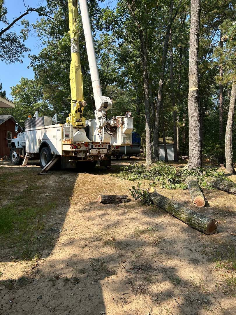 A white truck with a yellow crane is parked in a driveway next to trees.