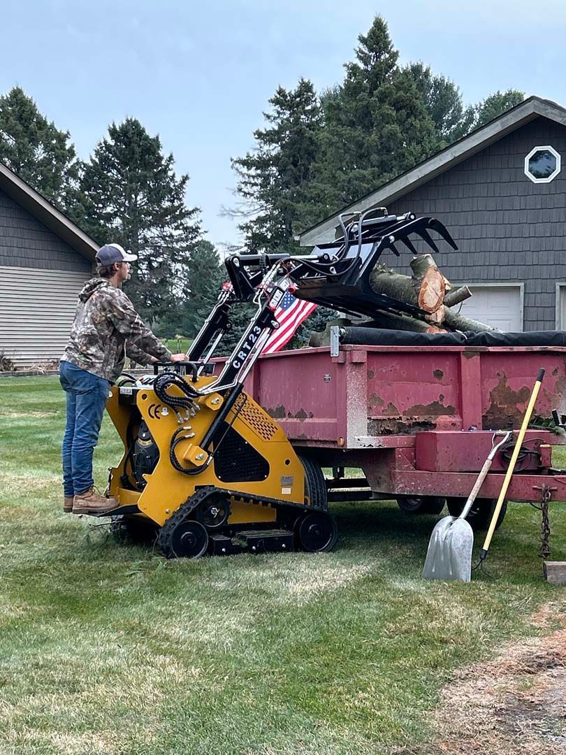 A man is loading logs into a trailer with a tractor.