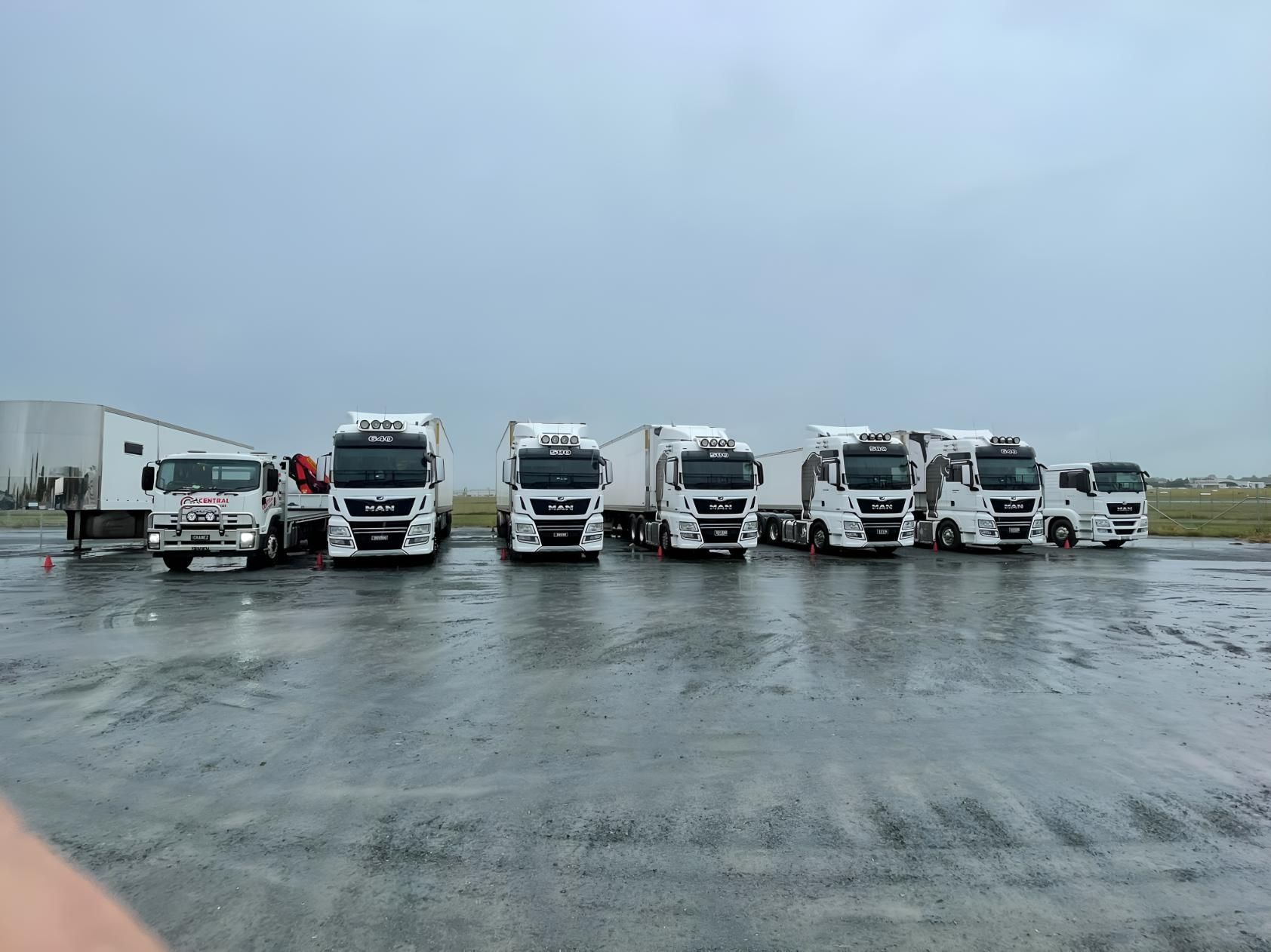 A Row of White Trucks Are Parked in a Parking Lot on a Rainy Day — Central Crane Trucks In Stapylton, QLD