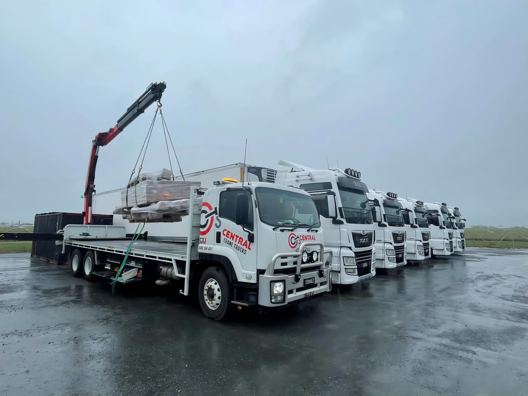 A Row of White Trucks Are Parked in a Parking Lot on a Rainy Day — Central Crane Trucks In Stapylton, QLD