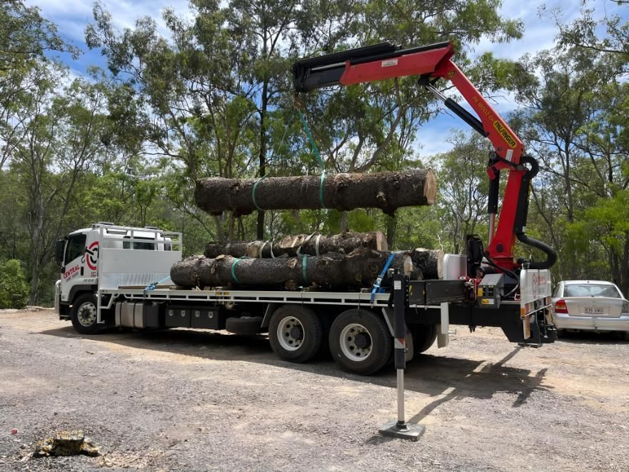 A Truck With a Crane on It is Carrying Logs in a Parking Lot — Central Crane Trucks In Stapylton, QLD