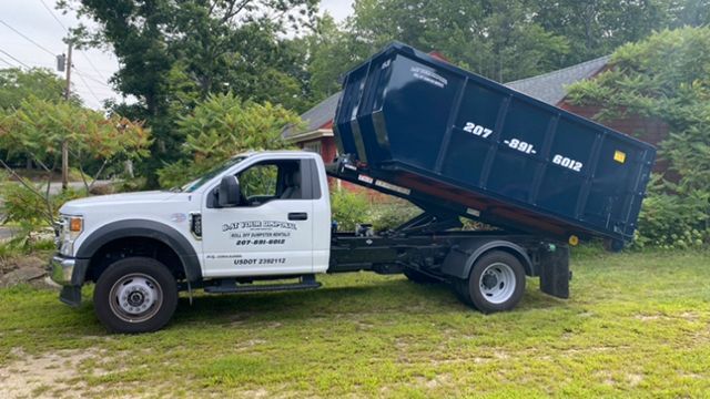 A dumpster truck is parked in a grassy yard next to a house.