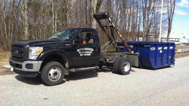 A black dump truck with a blue dumpster attached to it is parked on the side of the road.