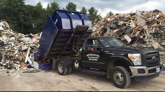 A dump truck is parked in front of a pile of trash.