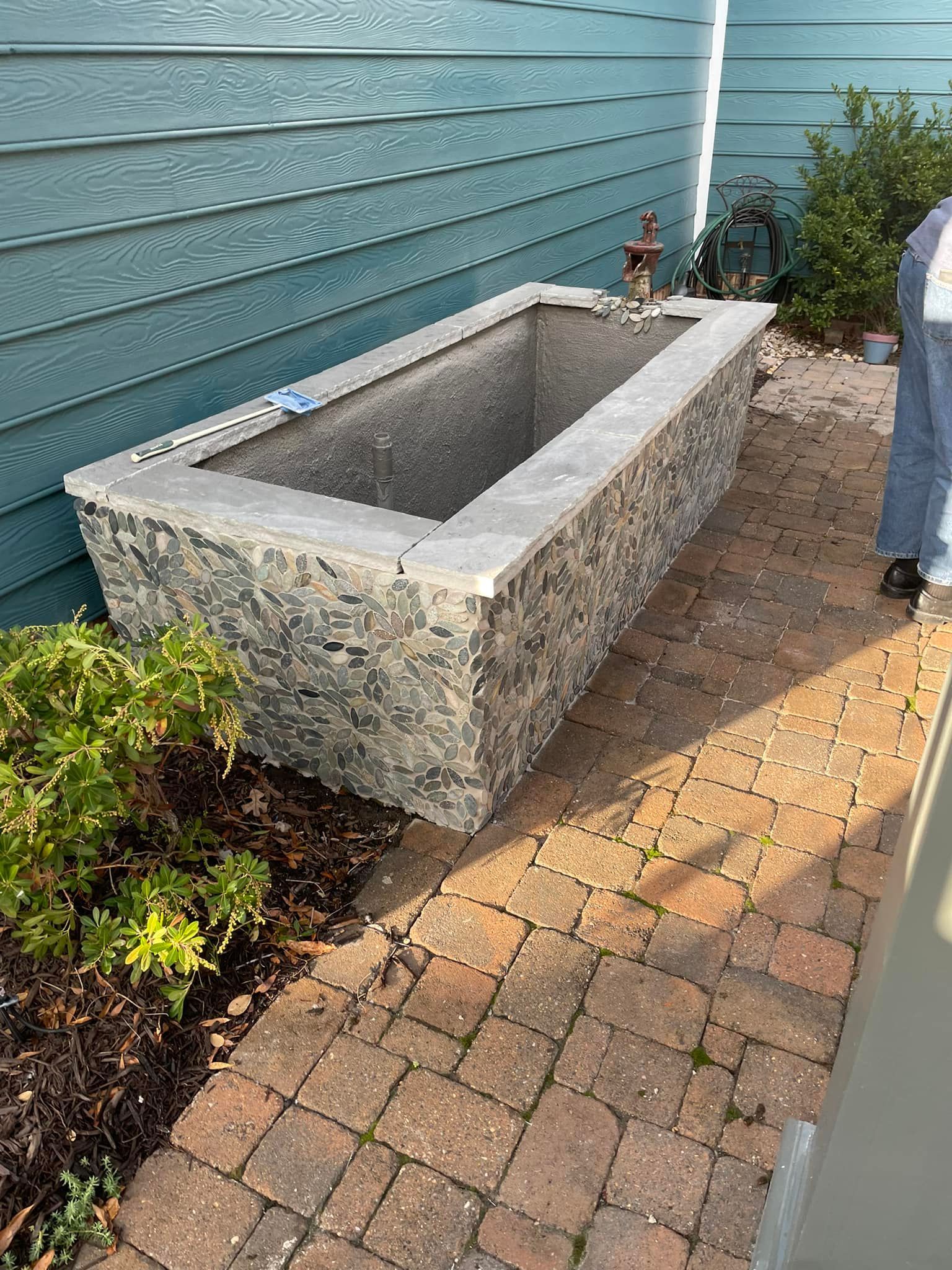 A large stone bathtub is sitting on a brick walkway next to a house.