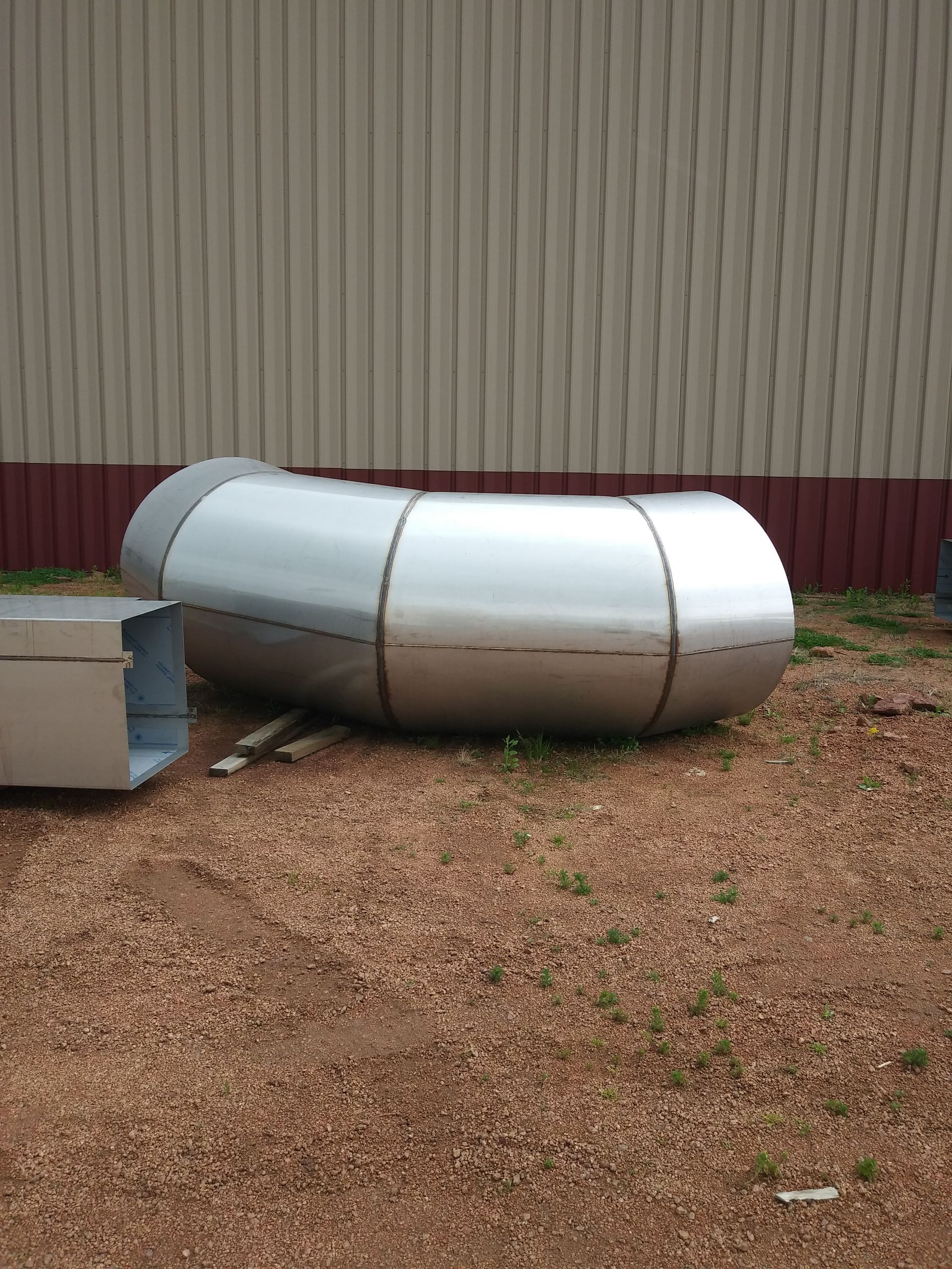 Silver metal pipe section lying on a bed of brown gravel outside a tan building.