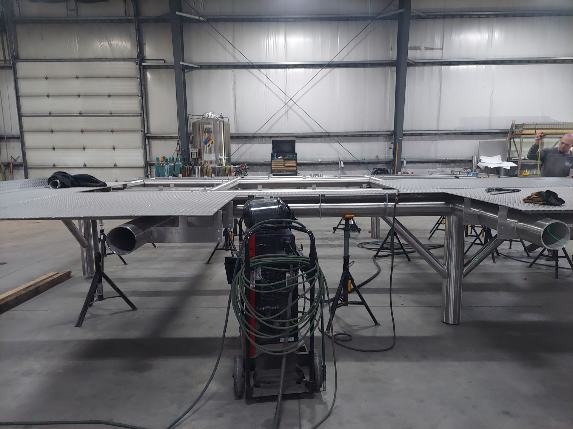 Welding table under construction in a warehouse, with a welding machine in the foreground.