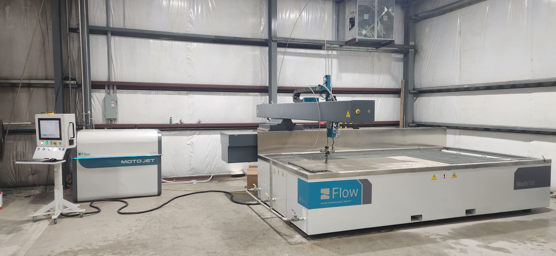 A waterjet cutting machine in a large industrial setting. The machine is teal and white with a