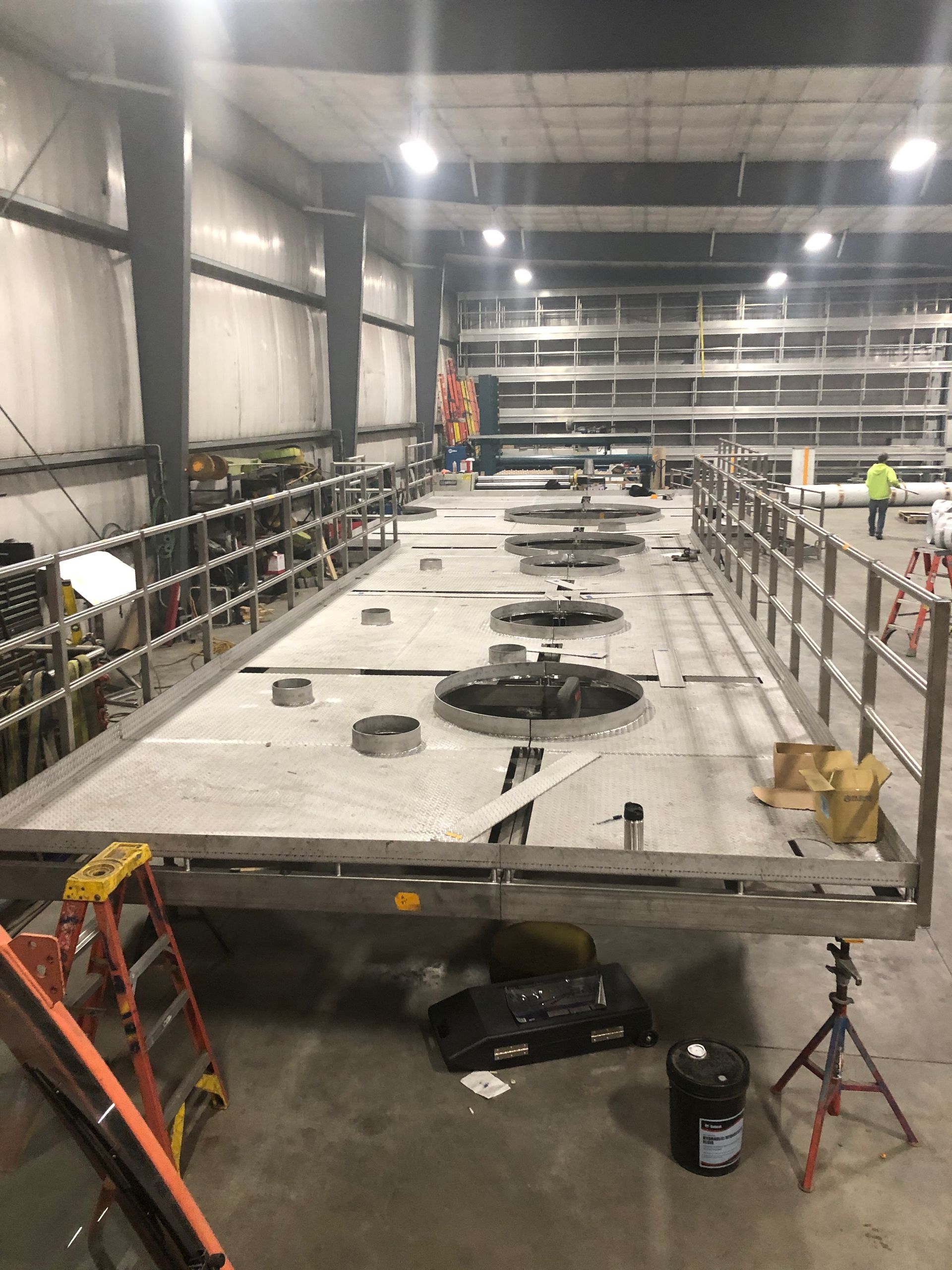 Large industrial tank under construction inside a warehouse, featuring safety railings and various openings.
