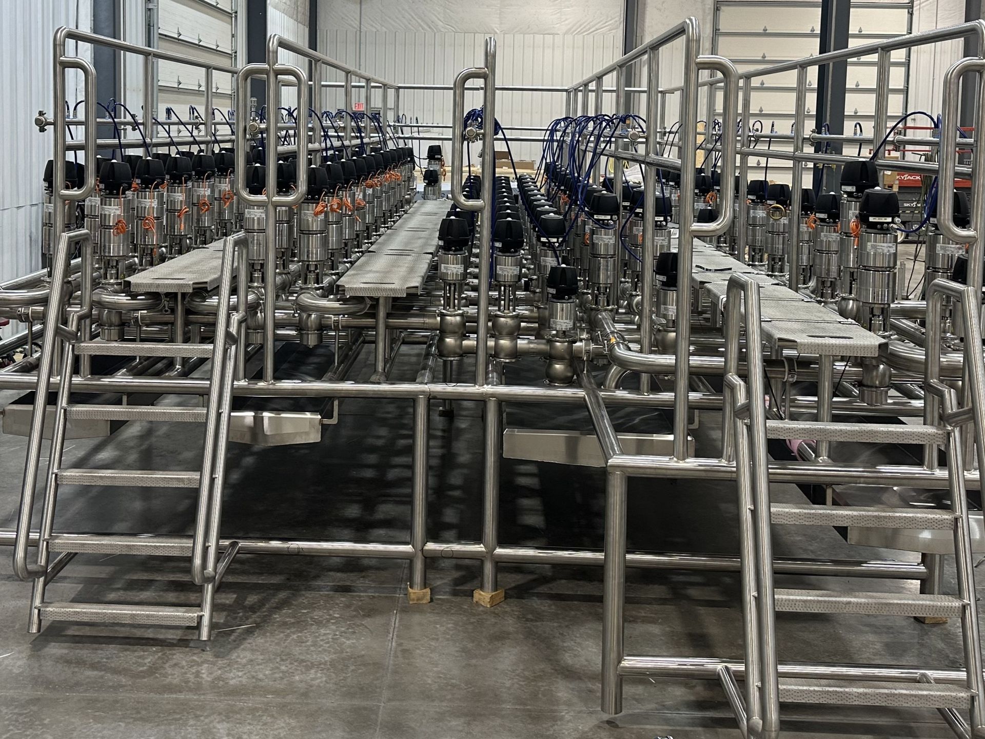 Stainless steel industrial piping with multiple valves and platforms in a warehouse.