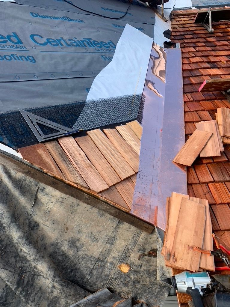 Cedar shingle roof repair with exposed underlayment and a white flashing strip