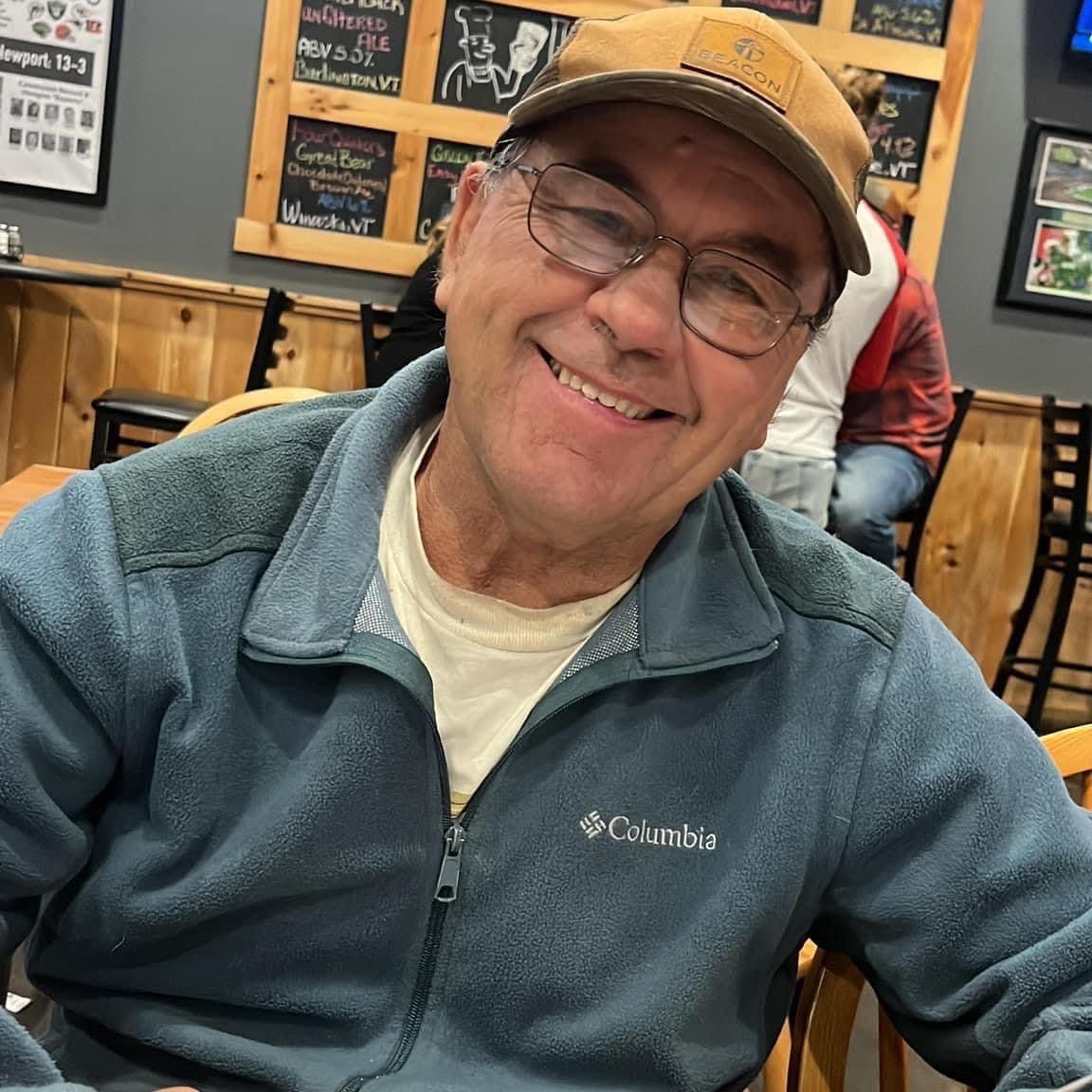 A man wearing glasses and a columbia jacket smiles for the camera