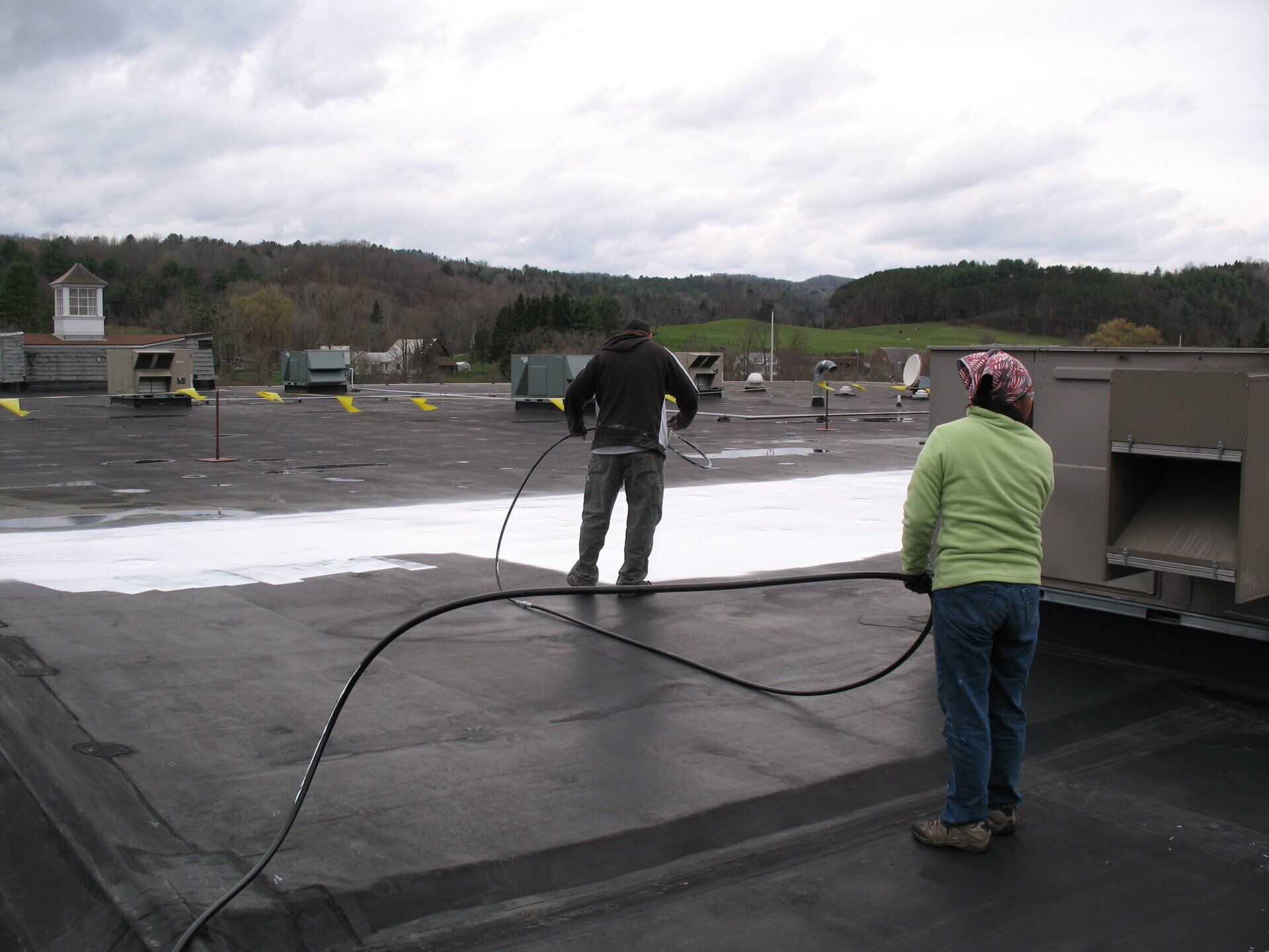 A man and a woman spraying a roof with a hose