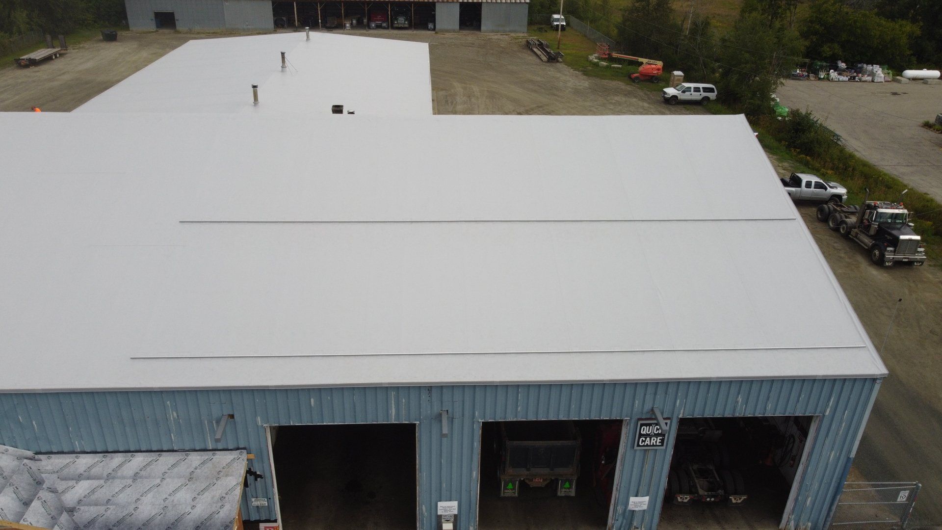 Aerial view of Rodd Roofing’s large metal retrofit project with a vast, flat white roof and adjacent parking.