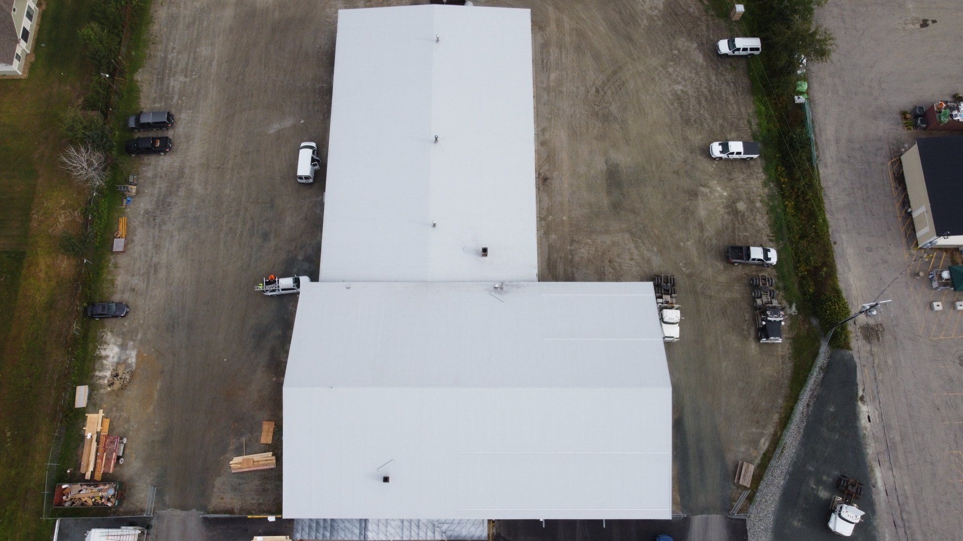 Aerial view of a large, flat white roof by Rodd Roofing, with vehicles and materials nearby, indicating a retrofit project.
