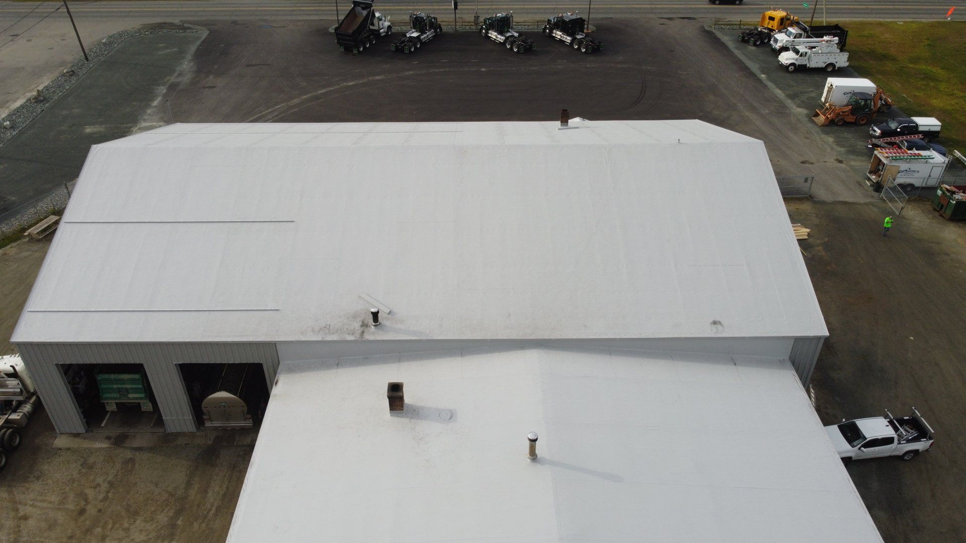 Aerial view of a flat white roof, likely a retrofit project by Rodd Roofing, with vehicles and equipment nearby.