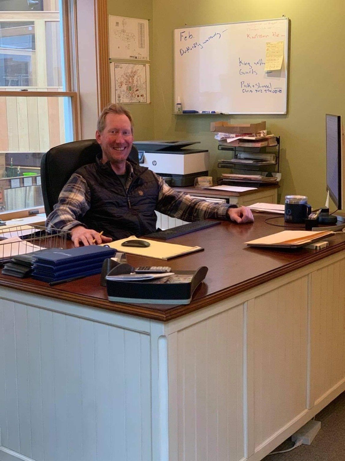 A man is sitting at a desk in front of a whiteboard that says ' i 'm sorry ' on it