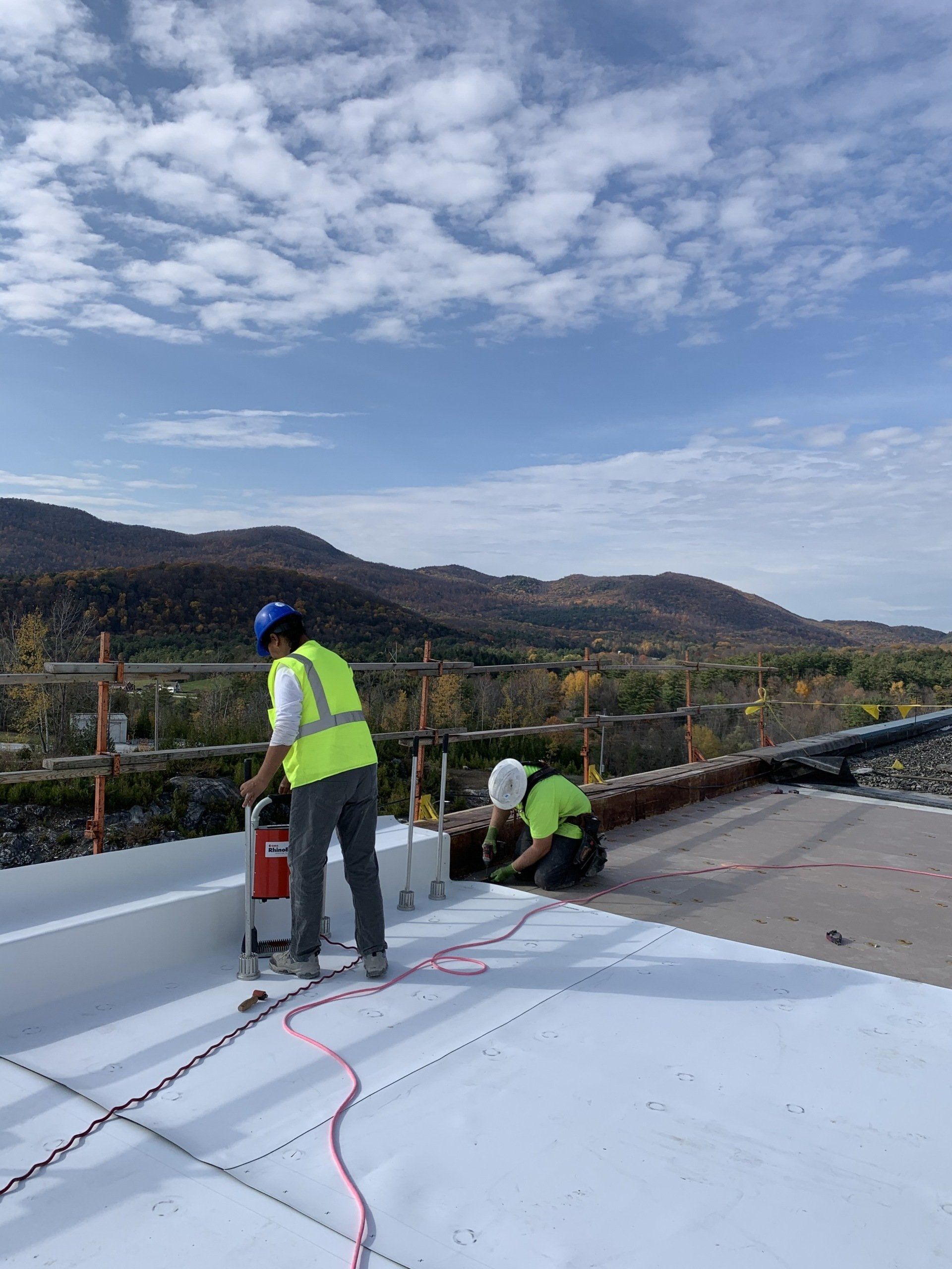 Two construction workers are working on a white roof.