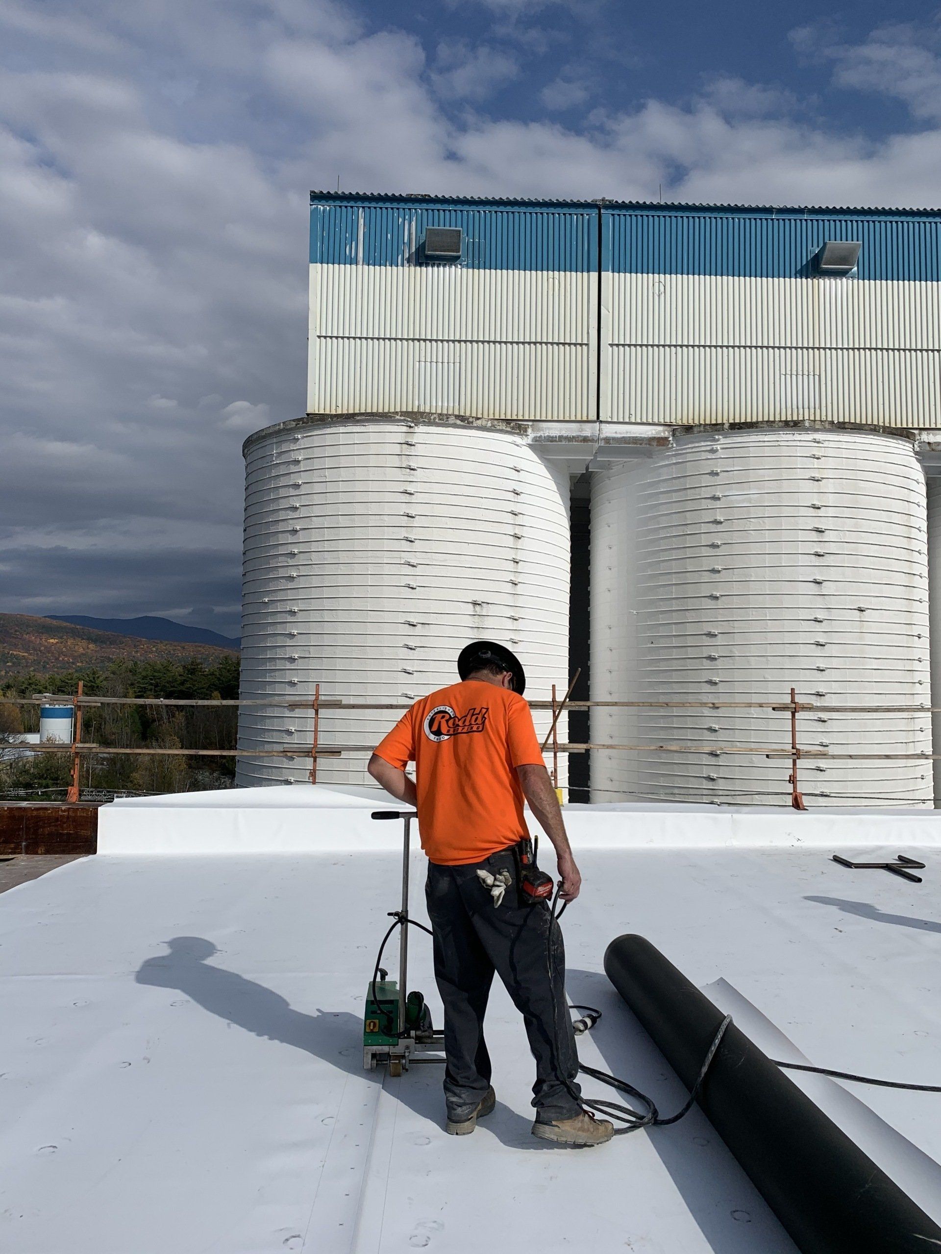 A man in an orange shirt is working on a white roof.