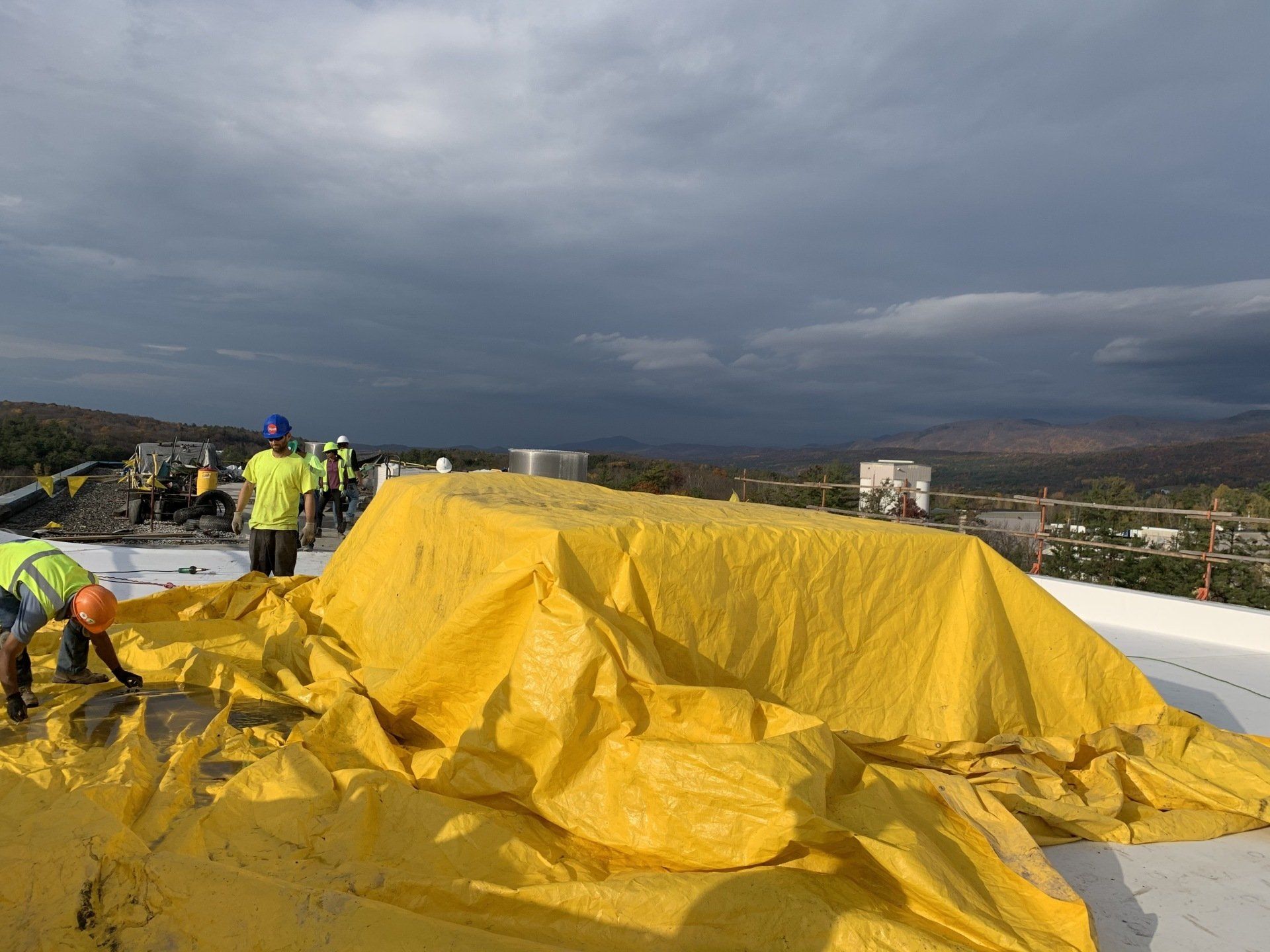 A group of construction workers are covering a roof with a yellow tarp.