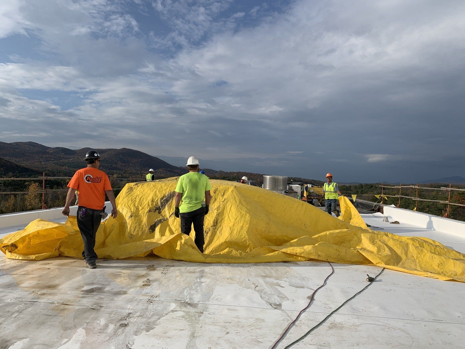 A group of construction workers are walking on top of a white roof.